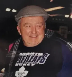 Smiling man wearing Toronto Maple Leafs shirt and cap.