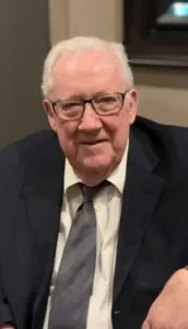 Elderly man in suit with glasses smiling indoors.