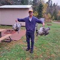 Man holding two wild game birds outdoors.