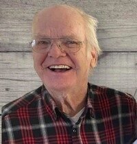 Smiling elderly man in plaid shirt with glasses.