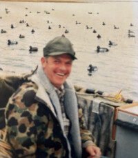 Smiling man in boat with ducks on lake.