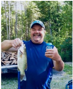 Man holding fish and beverage outdoors.