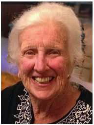 Smiling elderly woman with white hair, embroidered blouse.
