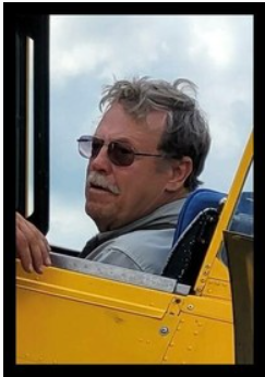 Man in yellow plane looking out window.