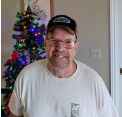 Smiling man in cap near decorated Christmas tree.