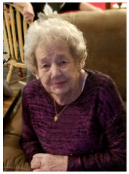 Elderly woman sitting on brown couch, smiling.