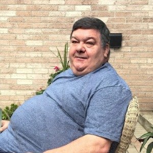 Man sitting outside, smiling by brick wall.