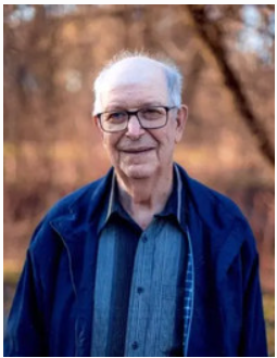 Smiling elderly man outdoors in a blue jacket.