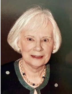 Elderly woman smiling, wearing black and pearl necklace.