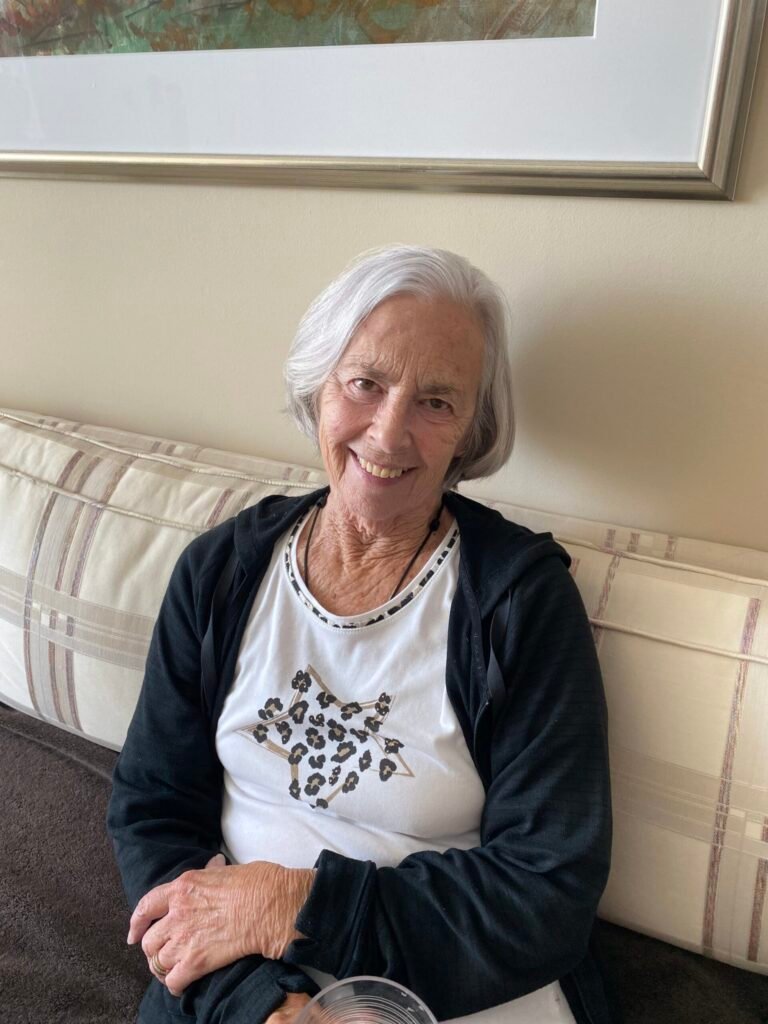 BRUNNER, Muriel Brunner Smiling elderly woman sitting on a couch.