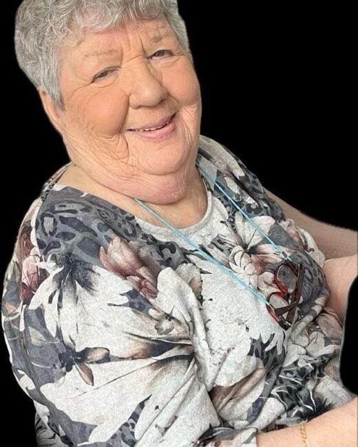 Smiling elderly woman in floral shirt.