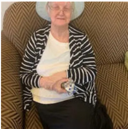 Elderly woman sitting on patterned couch, holding remote.