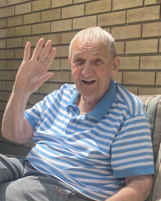 Elderly man smiling and waving at camera.