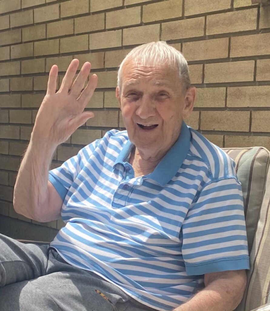 Elderly man smiling and waving at camera.