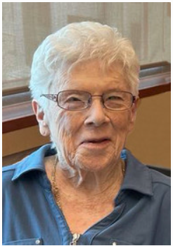 Elderly person smiling, wearing glasses and blue shirt.