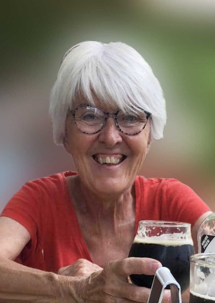 Smiling person holding a glass of dark beer.