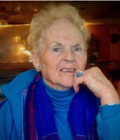 Elderly woman sitting, wearing blue jacket and scarf.