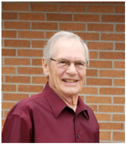Smiling man in red shirt, brick wall background.