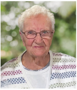Elderly woman smiling outdoors with blurred background.