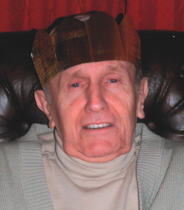 Elderly man wearing a paper crown, smiling indoors.