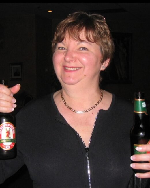 Person smiling, holding two beer bottles indoors.
