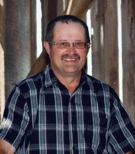 Smiling man in checkered shirt inside wooden structure.