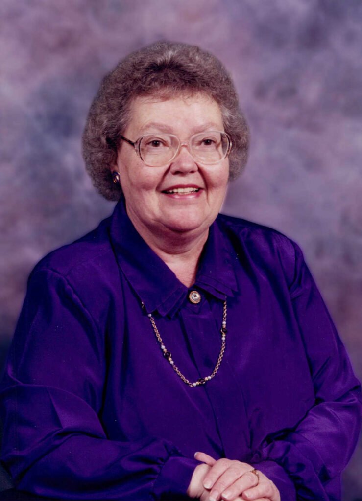 Elderly woman in purple shirt smiling.
