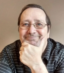 Smiling man with glasses and beard, hand on chin.