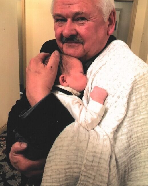 Elderly man holding a newborn baby lovingly.