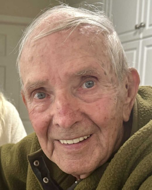Smiling elderly man in green jacket indoors.