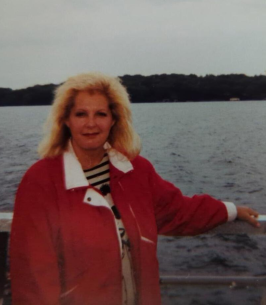 Person with blonde hair by a lake, cloudy sky.