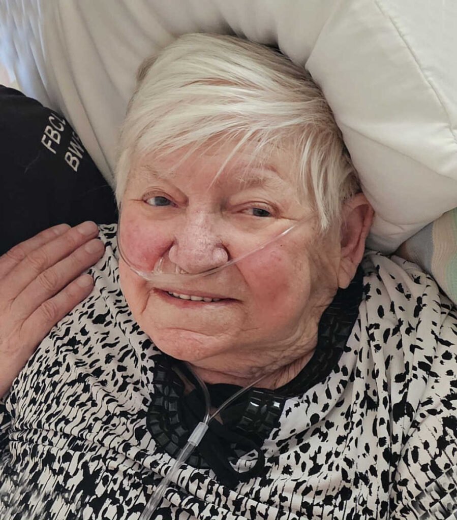 Elderly woman smiling with oxygen tube in hospital.