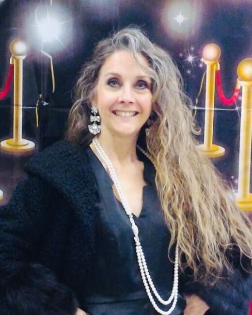 Smiling woman in black coat, red carpet backdrop
