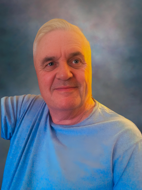 Smiling man wears light blue shirt against blue background.