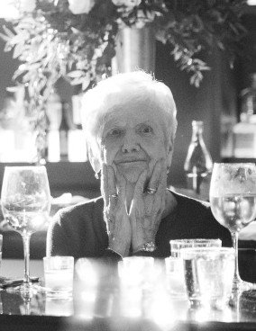 Elderly woman sitting at table with glassware.