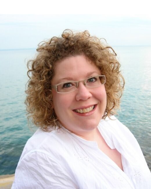 Smiling person beside ocean wearing glasses.
