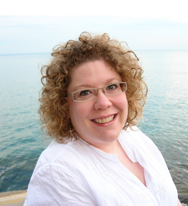Smiling person beside ocean wearing glasses.