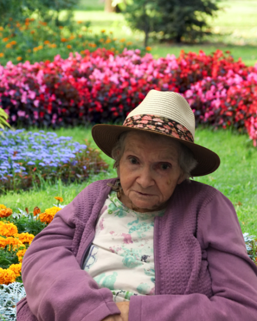 Elderly woman in hat seated in vibrant garden.