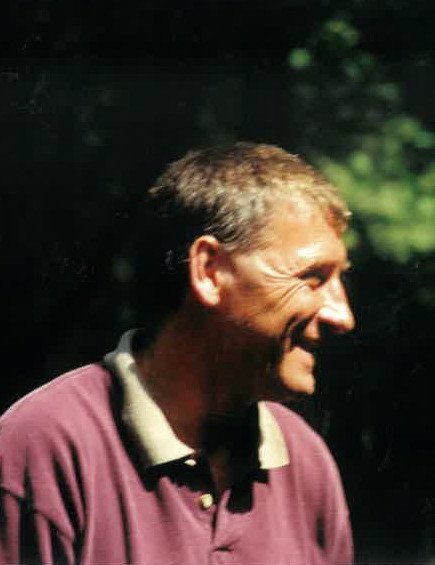 Smiling man in a purple shirt outdoors.