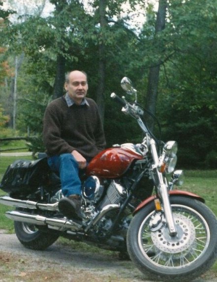 Man sitting on motorcycle in a park.