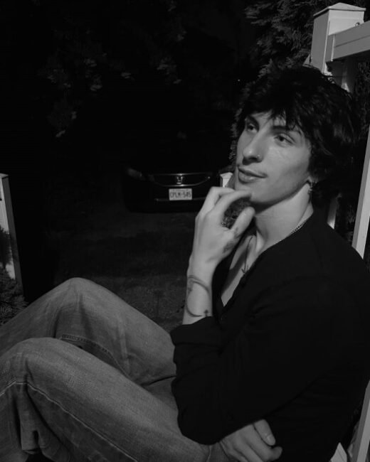 Person seated outdoors at night, thoughtful expression.