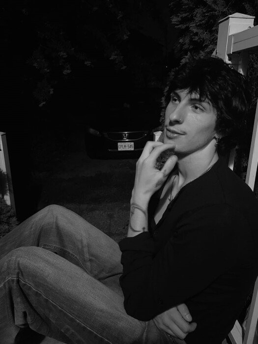 Person seated outdoors at night, thoughtful expression.