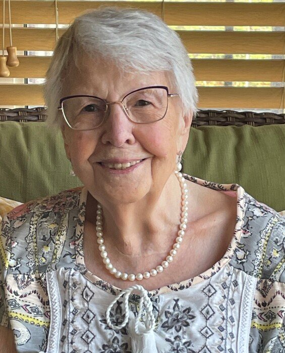Smiling elderly woman with glasses and pearl necklace.