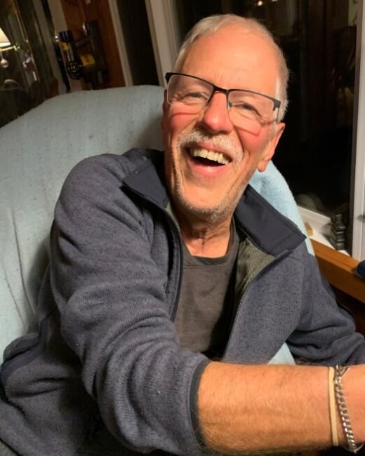 Smiling elderly person in casual attire indoors.