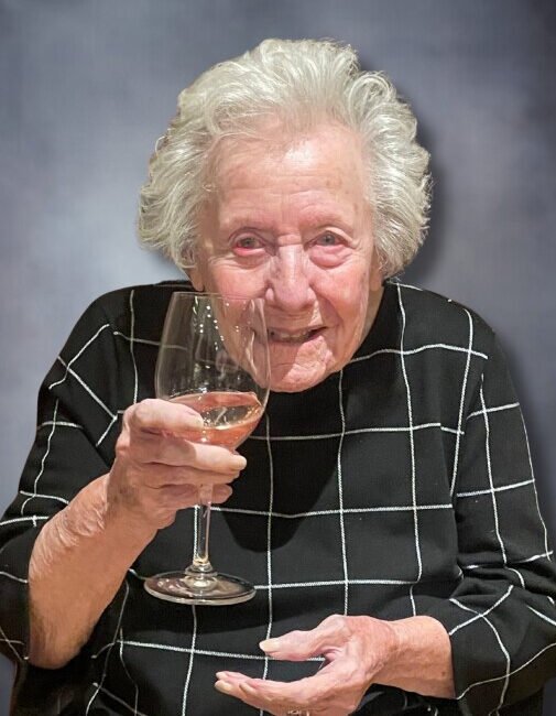 Elderly woman smiling and holding a wine glass.
