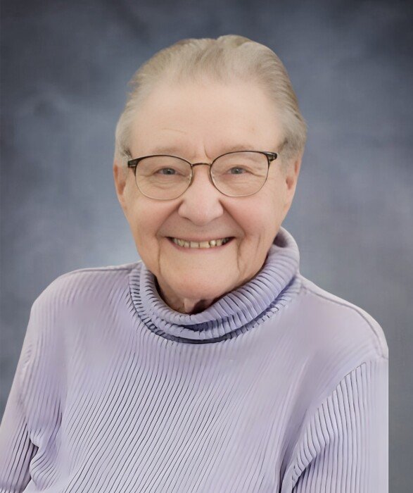 Smiling elderly person wearing glasses and purple sweater.