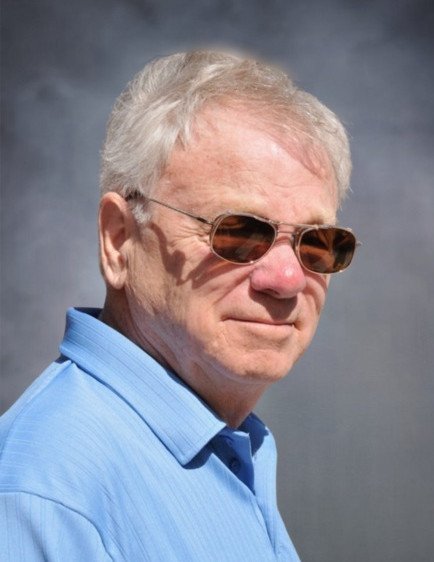 Elderly man in sunglasses, blue shirt, outdoor setting.