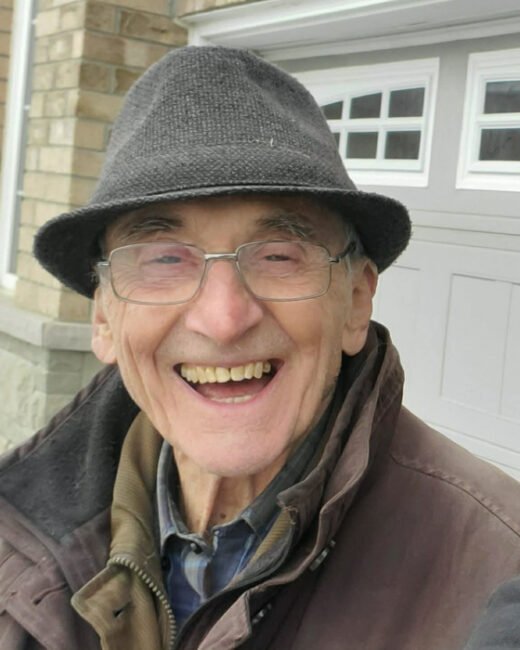 Smiling elderly man wearing glasses and hat outside.