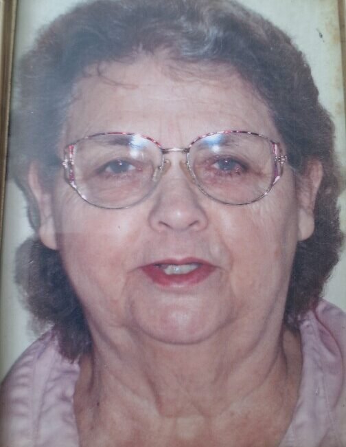 Elderly woman wearing glasses and a pink blouse.