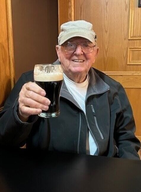 Elderly man holding a glass of dark beer.